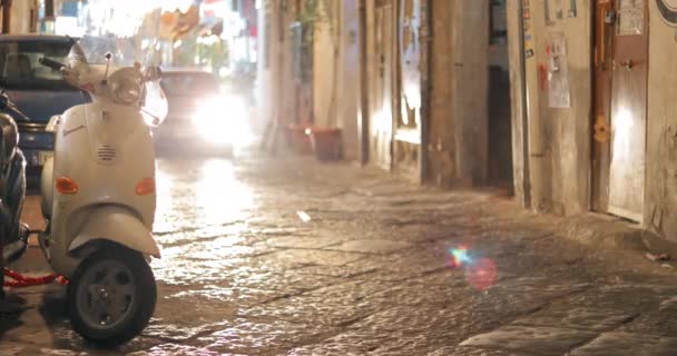 Napels, Italië - 18 oktober 2018: Auto rijden in de buurt van geparkeerde Vespa Scooter In Night Narrow Street. Vespa is een Italiaans merk van scooter vervaardigd door Piaggio — Stockvideo