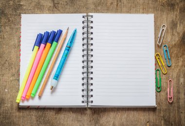 Defter kalem, kalem, renkli kalemler ve ahşap masa üzerinde ataç ile