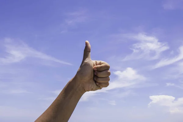 Male hand showing thumb up sign on blue sky background.