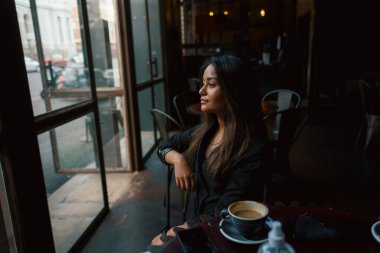 Genç melez kız kahve masasında oturuyor. 