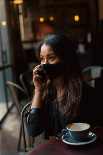 กสาวผสมเช อชาต ในหน ากากด วยสมาร ทโฟนและน บกาแฟ — ภาพถ่ายสต็อก
