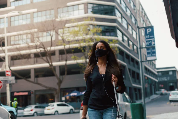 街の路上で音楽を聞いて顔のマスクを身に着けている若い女性 ロイヤリティフリーのストック画像