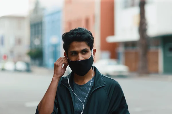 街の路上で音楽を聞いて顔のマスクを身に着けている若い男 ロイヤリティフリーのストック写真