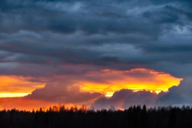 Nehir kıyısındaki gök gürültülü bulutların arasından gün batımı ışığı.