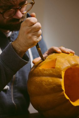 Cadılar bayramı için balkabağına surat oyan genç adam.