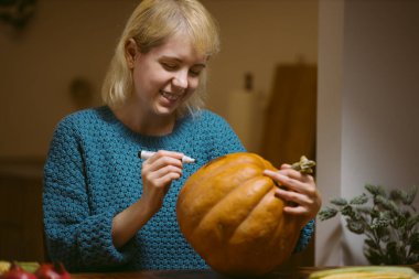 Cadılar bayramı için balkabağına surat çizen genç kadın.