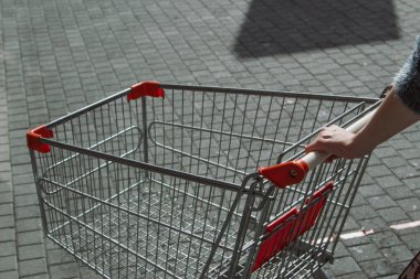 Bir kadının elleri boş alışveriş arabasını dışarı iterken yakın çekim.