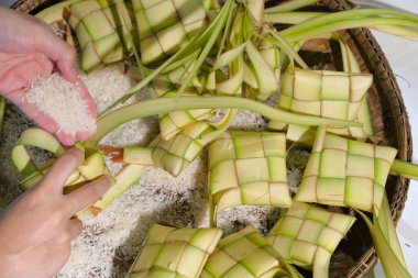 Ketupat kaplamasına pirinç dolduran eller. Ketupat, Güneydoğu Asya 'da festival sezonunda yerel bir lezzettir. Seçici odak.