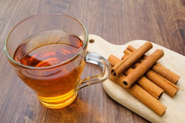 Ahşap masa arkasında tarçın çubukları olan bir bardak çay..
