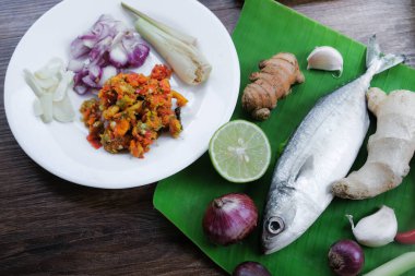 Ikan Pepes yapmak için baharatlı uskumru ya da ahşap masada muz yapraklarına sarılmış ızgara balık..