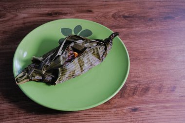 Ikan pepleri, yeşil tabakta muz yapraklarına sarılı ızgara balığı.