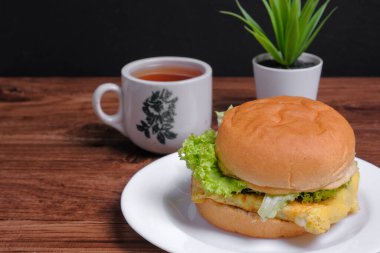 Yumurta burger ve ahşap zemin üzerinde bir fincan çay.