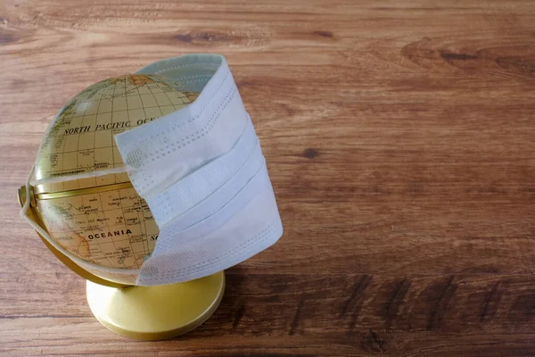 Globe  and face mask on wooden table. Covid-19 Coronavirus Outbreak concept