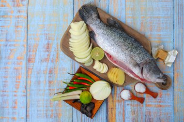 Ahşap kesim tahtasının üzerinde tuz, msg, zencefil, sarımsak, soğan, limon, biber ve limon otu ile Barramundi veya Asya deniz kabuğu balığı.