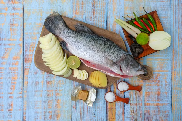 Ahşap kesim tahtasının üzerinde tuz, msg, zencefil, sarımsak, soğan, limon, biber ve limon otu ile Barramundi veya Asya deniz kabuğu balığı.