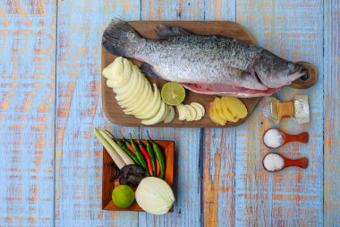 Ahşap kesim tahtasının üzerinde tuz, msg, zencefil, sarımsak, soğan, limon, biber ve limon otu ile Barramundi veya Asya deniz kabuğu balığı.