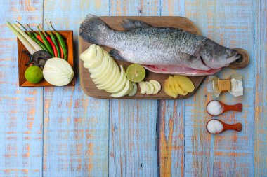 Ahşap kesim tahtasının üzerinde tuz, msg, zencefil, sarımsak, soğan, limon, biber ve limon otu ile Barramundi veya Asya deniz kabuğu balığı.