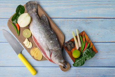 Bıçaklı, biberli, soğanlı, limonlu, kaffir limon yapraklı, zencefilli, sarımsaklı ve ağaç kesme tahtasının üzerinde yeşil limonlu Barramundi veya Asya deniz kabuğu balığı..