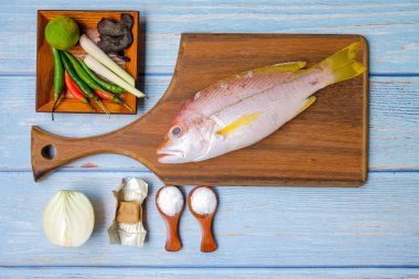 Tahta kesme tahtası, taze balık, tuz, zencefil, sarımsak, soğan, limon, biber ve ahşap arka planda limon otu..