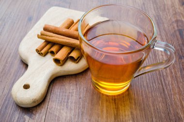 Ahşap masa arkasında tarçın çubukları olan bir bardak çay..