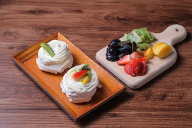 Krem şantili mini pavlovalar ve ahşap masada taze meyve.
