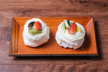 Krem şantili mini pavlovalar ve ahşap masada taze meyve.