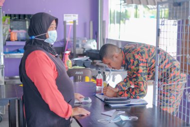  Asyalı garson koruyucu yüz maskesi takıyor. Müşteri sıcaklığını tarıyor.