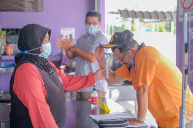 Muadzam Şah, Malezya - 22 Haziran 2020: Asyalı garson, Coronavirüs enfeksiyonunu önlemek için restorana girmeden önce termometreye kadar koruyucu yüz maskesi takıyor