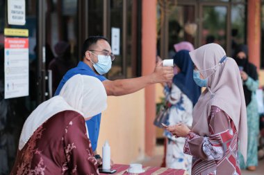 Muadzam Şah, Malezya - 29 Haziran 2020: Yeni normal, ofise girmeden önce sıcaklığı ölçmek için kızılötesi termometre kullanan erkekler. İnsanlar koruyucu maskeler takıyor, COVID-19 salgınını önlüyor
