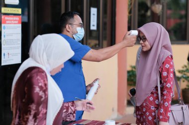 Muadzam Şah, Malezya - 29 Haziran 2020: Yeni normal, ofise girmeden önce sıcaklığı ölçmek için kızılötesi termometre kullanan erkekler. İnsanlar koruyucu maskeler takıyor, COVID-19 salgınını önlüyor