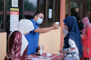 Muadzam Şah, Malezya - 29 Haziran 2020: Yeni normal, ofise girmeden önce sıcaklığı ölçmek için kızılötesi termometre kullanan erkekler. İnsanlar koruyucu maskeler takıyor, COVID-19 salgınını önlüyor