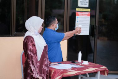 Muadzam Şah, Malezya - 29 Haziran 2020: Yeni normal, ofise girmeden önce sıcaklığı ölçmek için kızılötesi termometre kullanan erkekler. İnsanlar koruyucu maskeler takıyor, COVID-19 salgınını önlüyor