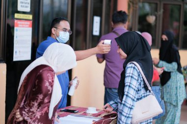 Muadzam Şah, Malezya - 29 Haziran 2020: Yeni normal, ofise girmeden önce sıcaklığı ölçmek için kızılötesi termometre kullanan erkekler. İnsanlar koruyucu maskeler takıyor, COVID-19 salgınını önlüyor