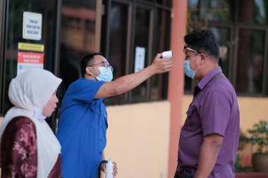 Muadzam Şah, Malezya - 29 Haziran 2020: Yeni normal, ofise girmeden önce sıcaklığı ölçmek için kızılötesi termometre kullanan erkekler. İnsanlar koruyucu maskeler takıyor, COVID-19 salgınını önlüyor