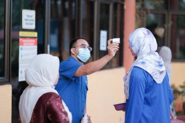 Muadzam Şah, Malezya - 29 Haziran 2020: Yeni normal, ofise girmeden önce sıcaklığı ölçmek için kızılötesi termometre kullanan erkekler. İnsanlar koruyucu maskeler takıyor, COVID-19 salgınını önlüyor