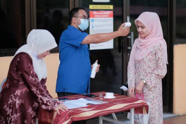 Muadzam Şah, Malezya - 29 Haziran 2020: Yeni normal, ofise girmeden önce sıcaklığı ölçmek için kızılötesi termometre kullanan erkekler. İnsanlar koruyucu maskeler takıyor, COVID-19 salgınını önlüyor