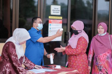 Muadzam Şah, Malezya - 29 Haziran 2020: Yeni normal, ofise girmeden önce sıcaklığı ölçmek için kızılötesi termometre kullanan erkekler. İnsanlar koruyucu maskeler takıyor, COVID-19 salgınını önlüyor