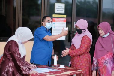 Muadzam Şah, Malezya - 29 Haziran 2020: Yeni normal, ofise girmeden önce sıcaklığı ölçmek için kızılötesi termometre kullanan erkekler. İnsanlar koruyucu maskeler takıyor, COVID-19 salgınını önlüyor