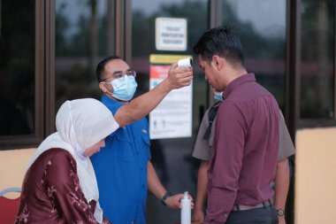 Muadzam Şah, Malezya - 29 Haziran 2020: Yeni normal, ofise girmeden önce sıcaklığı ölçmek için kızılötesi termometre kullanan erkekler. İnsanlar koruyucu maskeler takıyor, COVID-19 salgınını önlüyor