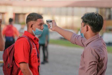 Öğrenci okula dönerken COVID-19 'un yayılması karşısında termometre ısısını ölçen öğrenciyi kullanıyor. Eğitim konsepti..