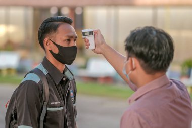Öğrenci okula dönerken COVID-19 'un yayılması karşısında termometre ısısını ölçen öğrenciyi kullanıyor. Eğitim konsepti..