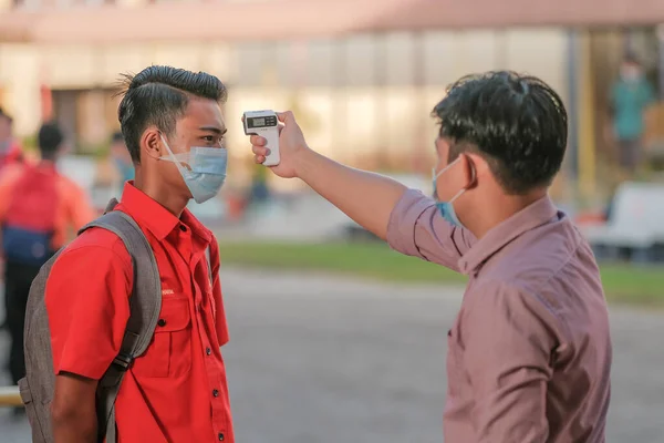 Öğrenci okula dönerken COVID-19 'un yayılması karşısında termometre ısısını ölçen öğrenciyi kullanıyor. Eğitim konsepti..