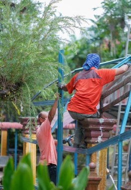 Muadzam Şah, Malezya - 15 Temmuz 2020: Kablosuz matkap ve vida kullanarak çatı için metal çatı işçiliği yapan inşaat işçileri. Endüstriyel kavram.