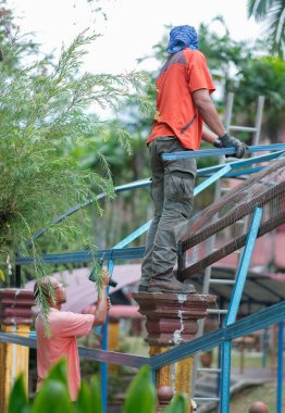 Muadzam Şah, Malezya - 15 Temmuz 2020: Kablosuz matkap ve vida kullanarak çatı için metal çatı işçiliği yapan inşaat işçileri. Endüstriyel kavram.