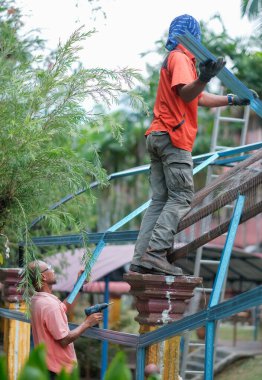 Muadzam Şah, Malezya - 15 Temmuz 2020: Kablosuz matkap ve vida kullanarak çatı için metal çatı işçiliği yapan inşaat işçileri. Endüstriyel kavram.