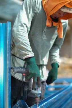 İnşaat işçisi inşaat alanında c kanalı çelik kirişleri takmak için elektrikli matkap ve vida aletleri kullanıyor. Endüstriyel kavram.