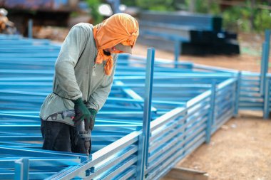 İnşaat işçisi inşaat alanında c kanalı çelik kirişleri takmak için elektrikli matkap ve vida aletleri kullanıyor. Endüstriyel kavram.