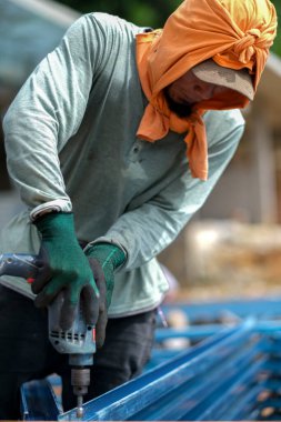 İnşaat işçisi inşaat alanında c kanalı çelik kirişleri takmak için elektrikli matkap ve vida aletleri kullanıyor. Endüstriyel kavram.