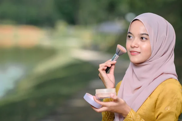 Asean woman applying makeup on her face, wearing traditional Malay  dress.