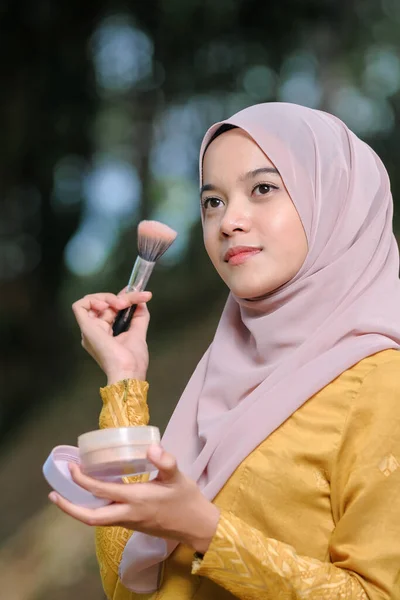 Asean woman applying makeup on her face, wearing traditional Malay  dress.